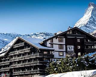Hotel building in front of a snow-covered mountain peak in an alpine landscape