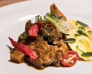 Fein angerichtetes Gericht mit Fleisch, Pasta und Gemüse auf weißem Teller.