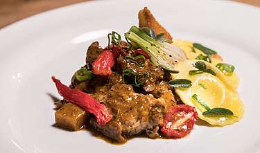 Anrichtetes Gourmetgericht mit Fleisch, Gemüse und Sauce auf weißem Teller.