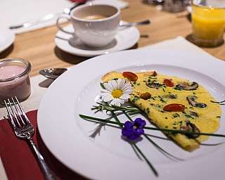 Omelette sur une assiette blanche décorée de fleurs, à côté du yaourt et des boissons sur la table.