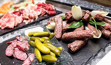 Différentes sortes de saucisses et de viandes sur des assiettes sombres avec des cornichons