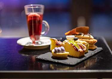 Verre de thé et différents petits desserts sur un plateau noir.