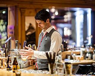 Ein Barkeeper zapft ein Getränk an einer Bar mit Gläsern und Flaschen.