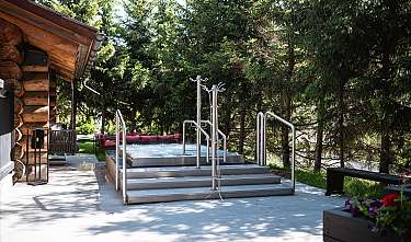 Bain à remous extérieur avec garde-corps en acier inoxydable à côté d’une cabane en bois dans la forêt.