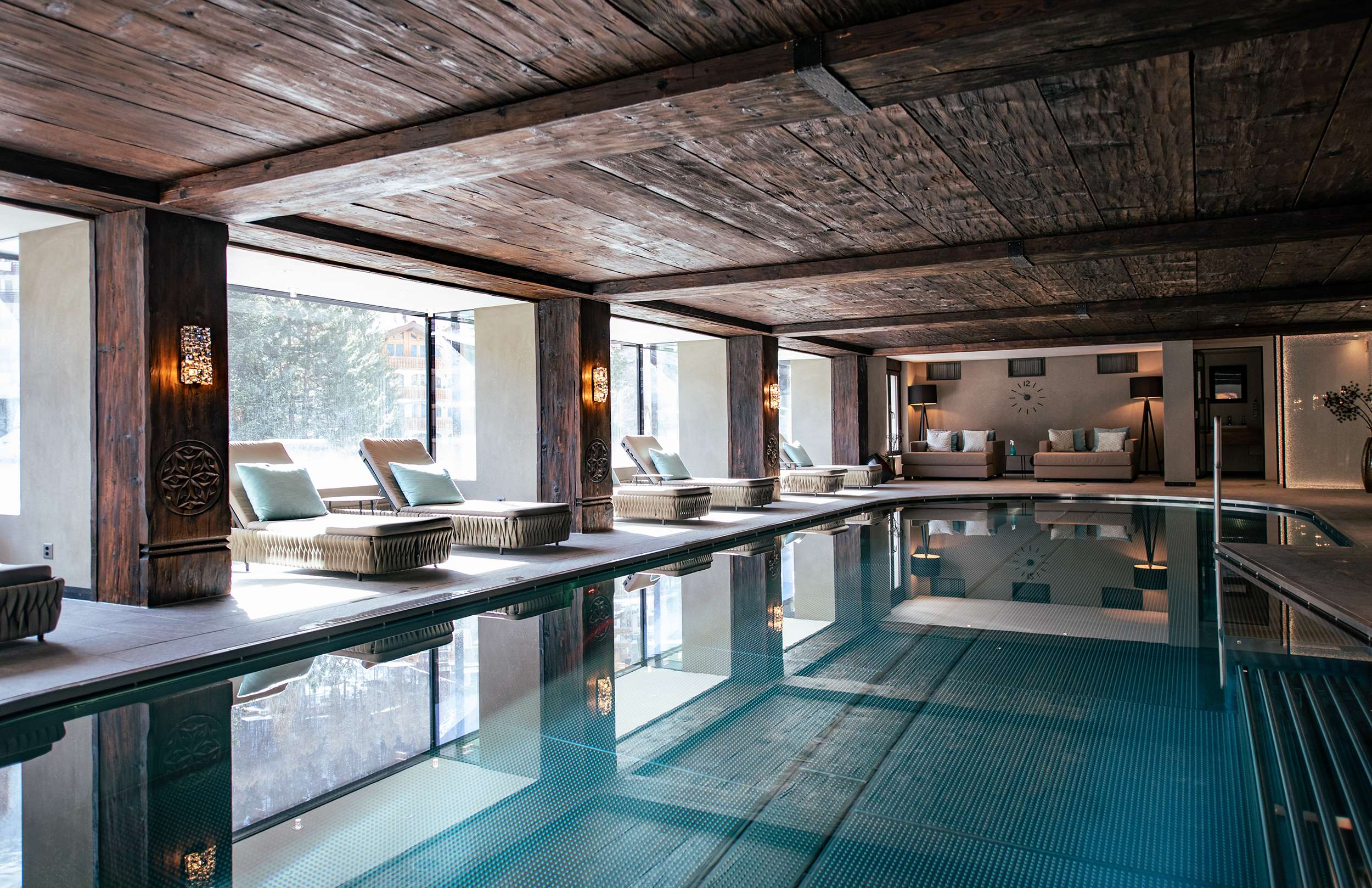 Moderner Innenpool mit Holzdecke, großen Fenstern und mehreren Liegen am Beckenrand.