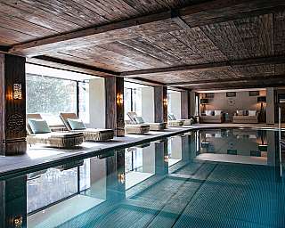 Indoor pool with wooden ceiling, loungers by the poolside and large windows in a modern spa area.