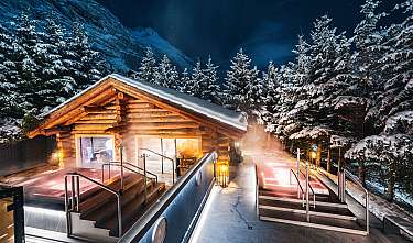 Holzhütte mit beleuchteten Außenbecken in verschneiter Berglandschaft bei Nacht
