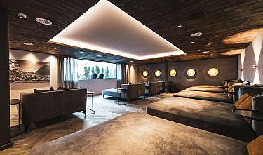 Salle lounge moderne et confortable avec canapés, fenêtres laissant entrer la lumière du jour et éclairage chaleureux.