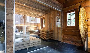 Sauna moderne avec revêtement en bois, parois vitrées, bancs et sol sombre carrelé.