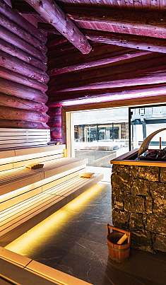 Intérieur d'un sauna en bois avec des bancs éclairés et un bassin en pierre.