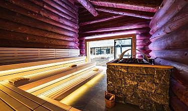 Intérieur d'un sauna en bois avec bancs éclairés et poêle habillé de pierre.