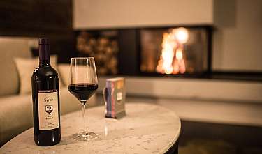 Bouteille de vin, verre de vin rempli et feu de cheminée sur une table.