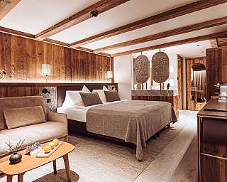 Chambre moderne avec poutres en bois, lit double, canapé et éléments d’éclairage chaleureux.