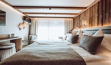 Chambre moderne avec grand lit, lambris en bois, rideaux clairs et lumière chaleureuse.