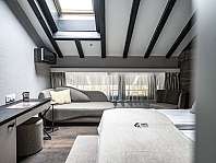 Modern eingerichtetes Schlafzimmer mit Sofa, Bett und sichtbaren Deckenbalken.