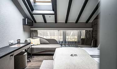 Helles modernes Schlafzimmer mit Bett, Sofa, Sessel und Dachfenster.