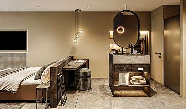 Modern eingerichtetes Schlafzimmer mit Bett, Schreibtisch, Waschbecken und warmem Licht.