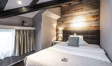 Modernes Schlafzimmer mit Bett, Holzwand, dunklem Kopfteil und Fenster mit Vorhängen.