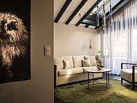 Helles Wohnzimmer mit Sofa, Sessel, Couchtisch, großem Schafbild und hohen Fenstern.