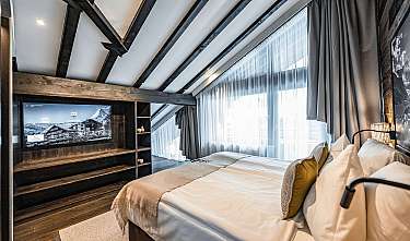 Cosy bedroom with large bed, television and floor-to-ceiling windows with curtains.