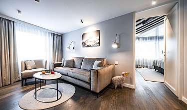Modernly furnished living room with grey sofa, armchair, coffee table and adjoining bedroom.
