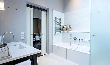 Bright modern bathroom with bathtub, washbasin and open door to the bedroom.