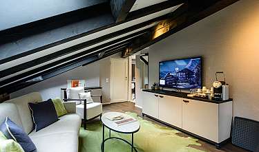 Modern hotel room with sofa, armchair, television, minibar and green carpet.