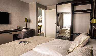 Modernly furnished hotel room with bed, desk, mirror and open wardrobe.