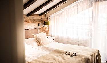Lit confortable dans une chambre lumineuse avec habillage en bois et grands rideaux.