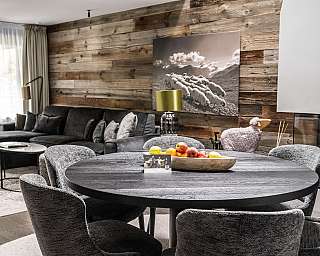 Modern living room with dark sofa, round dining table and wood panelling on the wall.
