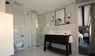 Salle de bains moderne avec douche vitrée, lavabo, toilettes et miroir à côté d'une porte ouverte.