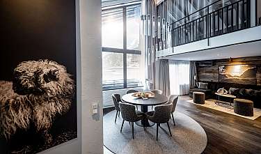 Salon et salle à manger modernes avec galerie, grande façade vitrée et mobilier sombre.