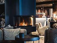 Gemütlicher Hotel-Loungebereich mit Kamin, Sessel und Rezeption im Hintergrund.