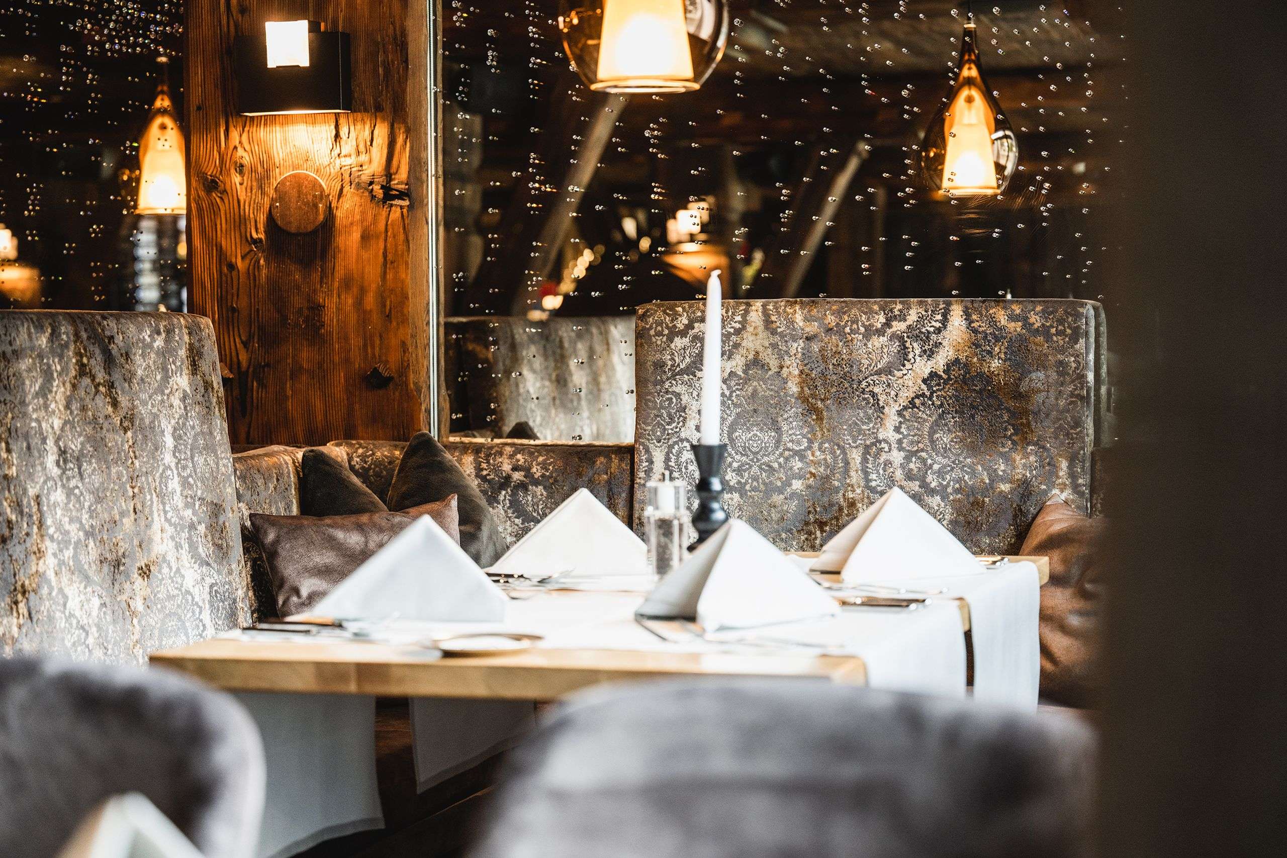 Ein stilvoll gedeckter Restauranttisch mit Kerze, Polsterbänken und warmen Pendelleuchten.