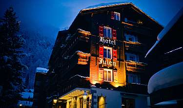 Bâtiment d'hôtel éclairé dans un paysage montagneux enneigé la nuit.