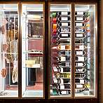 Beleuchteter Schrank mit Weinflaschen, Käse und hängenden Wurstwaren.