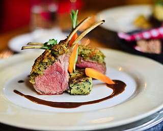 Gourmetgericht mit Lammrücken, Gemüse und Sauce auf einem weißen Teller.