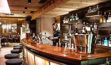Bar en bois confortable avec une barmaid, des étagères à bouteilles et des tabourets