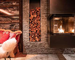Wohnzimmer mit brennendem Kamin, Holzstapel und rotem Sofa