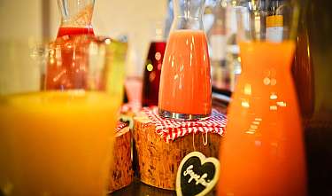 Several glass bottles with colourful fruit juices on wooden stands