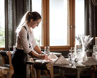 Kellnerin arrangiert Gläser und Servietten an einem elegant gedeckten Restauranttisch.