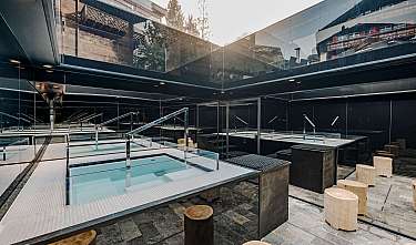 Spa moderne avec parois vitrées, bassin d’eau et tabourets d’assise en bois.