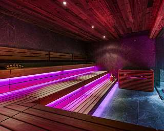 Intérieur d'un sauna moderne avec des banquettes en bois et un éclairage LED violet.