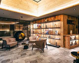 Moderne Lounge mit Sesseln, Kamin und Holzregalen in warmem Licht.