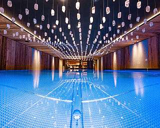 Eleganter Innenraum mit hängender Lichtinstallation über blau beleuchtetem Becken.