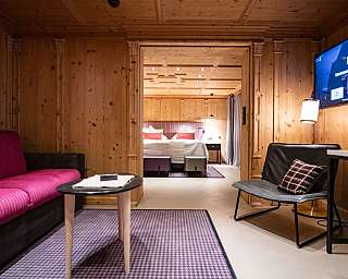 Chambre d'hôtel avec revêtement en bois, canapé, fauteuil, TV et vue sur la chambre à coucher
