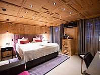 Chambre habillée de bois avec lit double, tables de chevet, tapis et grands rideaux.