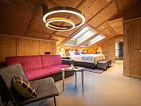 Chambre d'hôtel chaleureuse avec murs en bois, lit double, canapé et luminaire de plafond moderne.