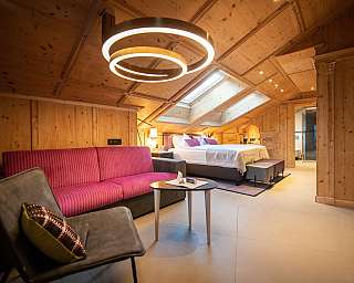 Chambre moderne avec habillage en bois, lit, canapé et plafonnier en forme d’anneau.
