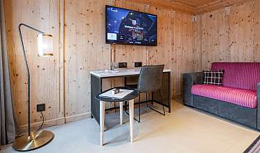 Chambre d'hôtel lambrissée de bois avec canapé, bureau, lampadaire et télévision murale.